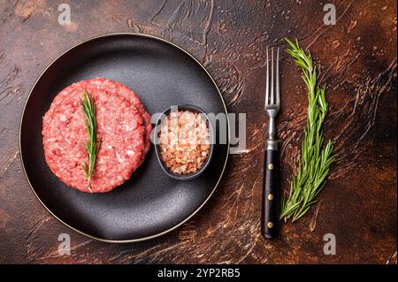 Rohe Kalb- und Rindfleisch Hackschnitzel für Burger mit Kräutern auf Teller. Brauner Hintergrund. Draufsicht. Stockfoto