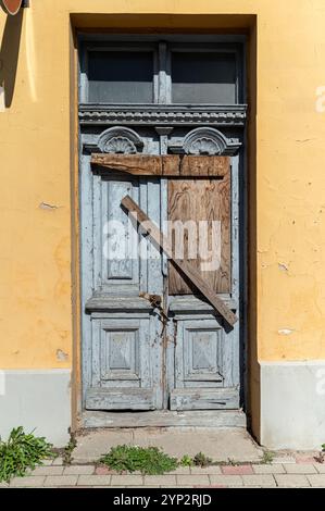 Eine alte blaue Tür mit Holzdielen, die sie kreuzen, steht auf einer hellgelben Wand. Stockfoto