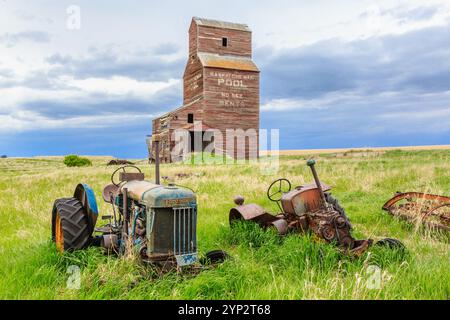 Zwei alte Traktoren sitzen auf einem Feld neben einem Kornsilo. Die Szene ist ruhig und friedlich, mit dem einzigen Knarren der alten Maschine Stockfoto