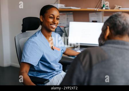 Glücklicher Arzt, der mit einem älteren Patienten spricht, während er auf Stuhl im Untersuchungsraum sitzt Stockfoto