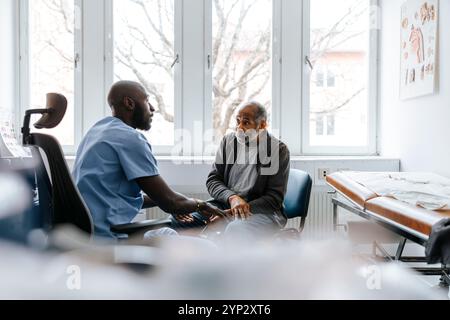 Älterer Mann, der von männlichem Gesundheitspersonal untersucht wird, während er im medizinischen Untersuchungsraum sitzt Stockfoto