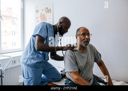 Männlicher Arzt überprüft den Rücken des älteren Mannes mit Stethoskop im Untersuchungsraum der Klinik Stockfoto