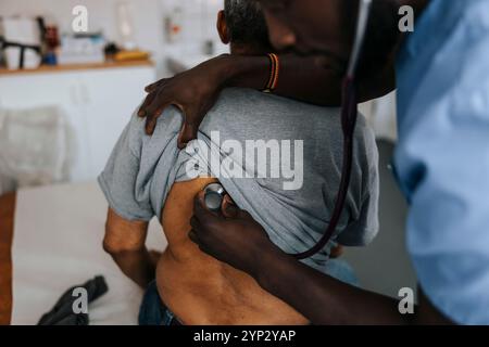 Männlicher Arzt, der den Rücken eines älteren Mannes mit Stethoskop im Untersuchungsraum der Klinik überprüft Stockfoto