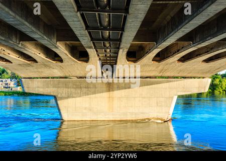 Von der Unterseite ist eine Brücke mit dem Wasser unten und dem Himmel darüber zu sehen. Die Brücke besteht aus Beton und hat ein Metallgeländer. Das Wasser ist kal Stockfoto