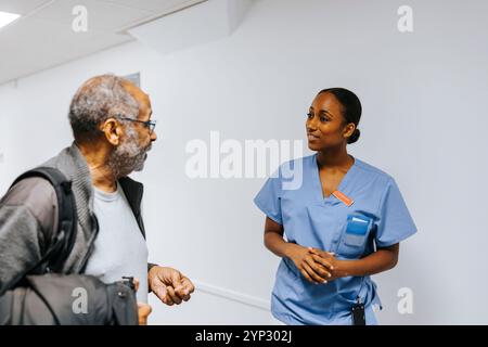 Junge Ärztin im Stehen und im Gespräch mit älteren Patienten auf dem Flur der Klinik Stockfoto