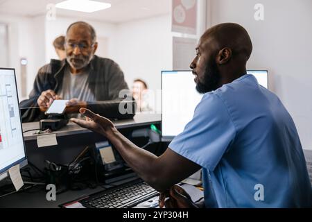 Senior Mann, der die Zahlung per Smartphone an der Rezeption in der medizinischen Klinik tätigt Stockfoto