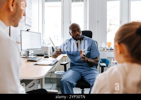 Männlicher Arzt, der Vater und Tochter im Untersuchungsraum des Krankenhauses erklärt Stockfoto