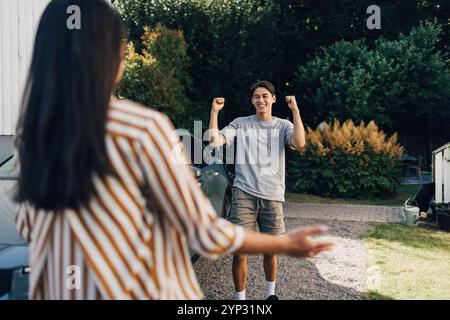 Fröhlicher junger Mann, der die Faust hält, während er mit Mutter im Hinterhof feiert Stockfoto