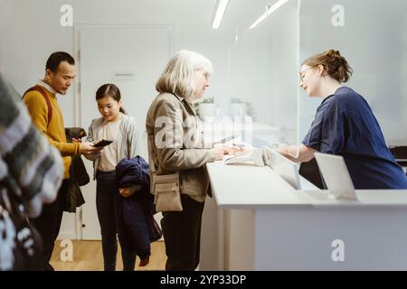 Weibliches medizinisches Personal, das ältere Frau beim Ausfüllen des Formulars während des Krankenhausbesuchs unterstützt Stockfoto