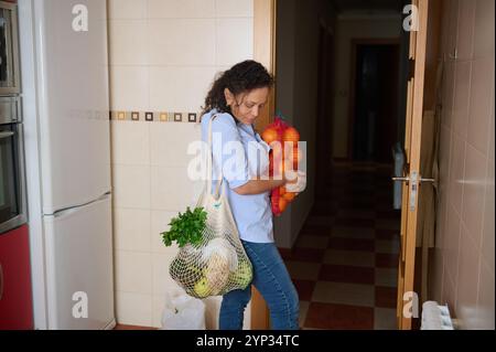 Eine Frau betritt ihre Küche mit frischen Produkten wie Orangen und grünem Gemüse. Die Szene vermittelt einen Fokus auf gesundes Leben und Nachhaltigkeit Stockfoto