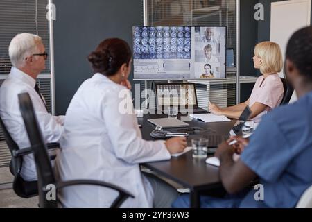 Professionelles Team von Radiologen, das an einem Online-Meeting mit Kollegen teilnimmt, die auf den Bildschirm schauen, mit Videokonferenz, während sie am Tisch in der Arztpraxis sitzen Stockfoto