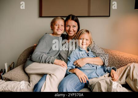Porträt einer lächelnden Frau, die zu Hause mit Söhnen auf dem Sofa sitzt Stockfoto