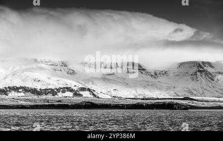 Schwarzweiß-Panoramafotos mit isländischer Küstenlandschaft. Schneebedeckte Berge liegen unter dramatisch bewölktem Himmel. Reykjavik und Umgebung, Island Stockfoto