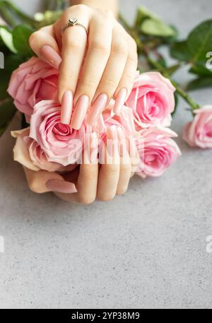 Hände einer Frau mit rosafarbener Maniküre, die zarte rosa Rosen hält und ihren Diamantring zeigt Stockfoto