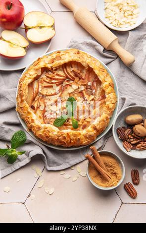 Frisch gebackene Apfelgalette mit Mandelflocken, Zimt und Minze, umgeben von Zutaten und Küchenutensilien Stockfoto