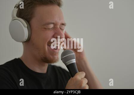 Ein Mann mit Kopfhörern, der emotional im Mikrofon singt. Stockfoto