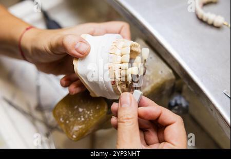Hände zur Einstellung einer Zahnprothese im Laborumfeld. Stockfoto