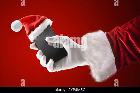 Weihnachtsmann Hand in Anzug und Handschuhe halten ein Smartphone mit einem Weihnachtsmann Hut auf isoliertem roten Hintergrund. Stockfoto