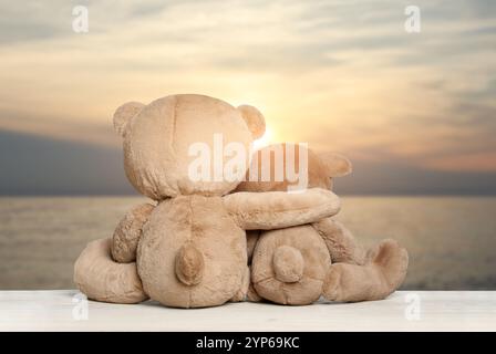 Umarmende Teddybären auf hölzernem Boden mit Blick auf die malerische Meereslandschaft, Rückansicht Stockfoto