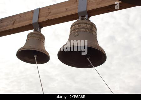 Zwei neue Bronzeglocken hängen von einem Holzbalken an einem bewölkten Himmel. Ein obligatorisches Element der orthodoxen Kirchen. Stockfoto