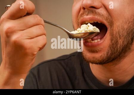 Ein Mann ist dabei, eine Handvoll Popcorn in einem Löffel zu genießen, wobei er sich auf die Details des Imbisses und den Moment der Mahlzeit konzentriert. Ideal für Snacks oder Unterhaltung Stockfoto