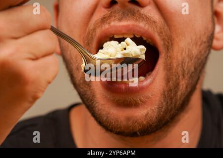 Ein Mann ist dabei, eine Handvoll Popcorn in einem Löffel zu genießen, wobei er sich auf die Details des Imbisses und den Moment der Mahlzeit konzentriert. Ideal für Snacks oder Unterhaltung Stockfoto