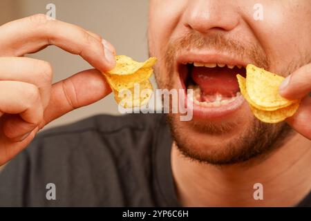 Nahaufnahme eines bärtigen Mannes, der knusprige Chips mit zwei Händen isst und sich auf Textur und Details konzentriert. Als Konzept für Snack-Aktionen. Bild einer mou eines Mannes Stockfoto