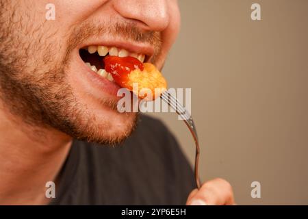 Eine Nahaufnahme einer Hand, die knusprige Nuggets auf einer Gabel hält, perfekt für die Darstellung des Genusses des Essens. Die Nuggets sind in rote Soße getaucht, Ketchup Stockfoto