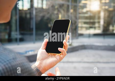 Smartphone mit leerem schwarzen Bildschirm in der Hand einer Geschäftsfrau auf der Straße der Stadt. Stockfoto