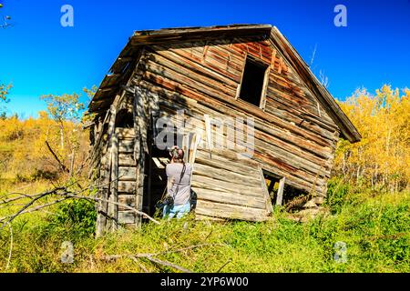 Eine Frau steht vor einem baufälligen alten Haus. Das Haus ist in einem Zustand des Verfallens, mit kaputten Fenstern und einem durchhängenden Dach. Die Frau ist lch Stockfoto