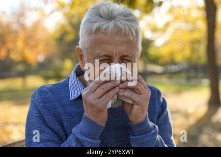 Seniorenmann mit Gewebe, das im Park eine laufende Nase bläst Stockfoto