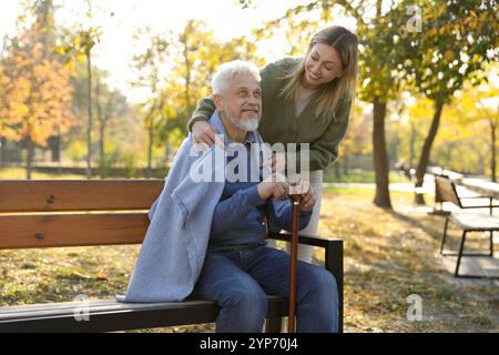 Betreuer, der Senioren auf Holzbank im Park hilft. Häuslicher Gesundheitsdienst Stockfoto