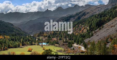 Landschaftsfotografie eines Tals am Col de VARs in den französischen Alpen, mit einem kleinen See in der Mitte und Lärchen in Herbstfarben, Panorama Stockfoto