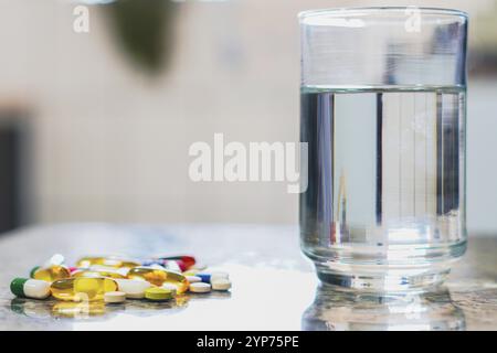 Ein paar Pillen auf dem Tisch neben einem Glas Wasser Stockfoto