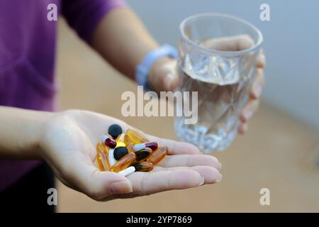 In dieser Abbildung befinden sich mehrere Medikamententabletten in der Hand einer Person und halten ein Glas Wasser Stockfoto