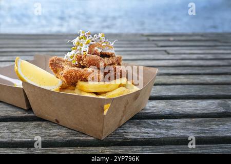 Fish and Chips mit Zitronenscheibe und Sprossen in einem Karton auf einem verwitterten Holzdock am Meer, Kopierraum, ausgewählter Fokus Stockfoto