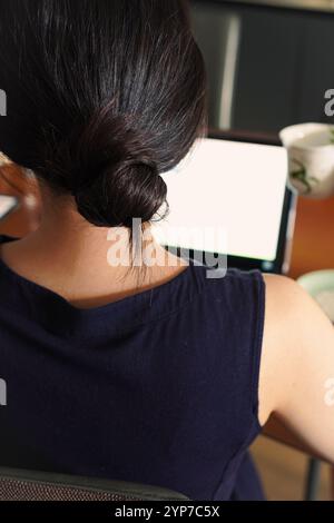Rückansicht einer jungen Geschäftsfrau, die mit einer Teetasse in der Hand an ihrem Laptop arbeitet Stockfoto