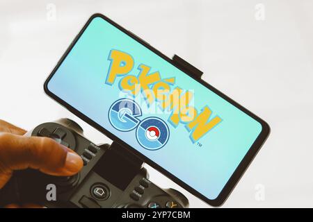 In dieser Fotoabbildung wird eine Person, die auf einem Joystick spielt, und das Pokemon GO-Logo auf einem Smartphone-Bildschirm angezeigt Stockfoto