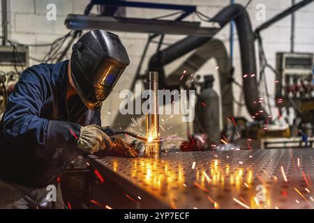 Nicht erkennbarer Schweißer mit Schutzmaske und Handschuhen, die ein Metallstück in einer Fabrik schweißen Stockfoto