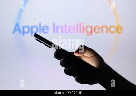 In dieser Fotoabbildung ist das Apple Intelligence Logo im Hintergrund einer Silhouettenhand zu sehen, die ein Smartphone hält Stockfoto