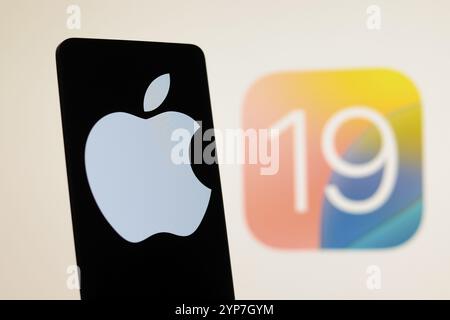 In dieser Fotoabbildung wird das Apple-Logo auf einem Smartphone mit einem iOS 19-Logo im Hintergrund angezeigt Stockfoto