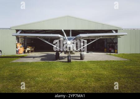 Ein kleines einmotoriges Flugzeug steht vor einem offenen Hangar auf einer Grasbahn in Dunedin, Neuseeland, Ozeanien Stockfoto