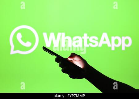 In dieser Fotoabbildung ist das WhatsApp-Logo im Hintergrund einer Silhouettenhand zu sehen, die ein Smartphone hält Stockfoto