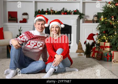 Schönes Paar in Weihnachtspullover und Weihnachtsmützen zu Hause Stockfoto