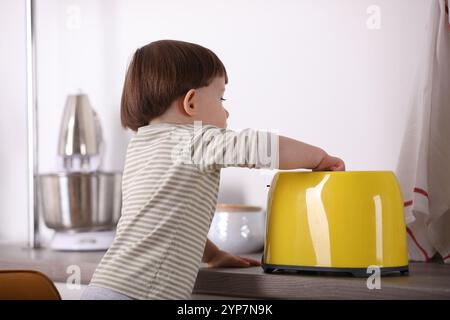 Kleiner Junge, der mit Toaster in der Küche spielt. Gefährliche Situation Stockfoto