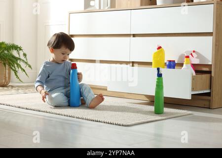 Kleiner Junge, der mit Waschmittelflaschen in der Nähe des Schranks zu Hause spielt. Kind in Gefahr Stockfoto