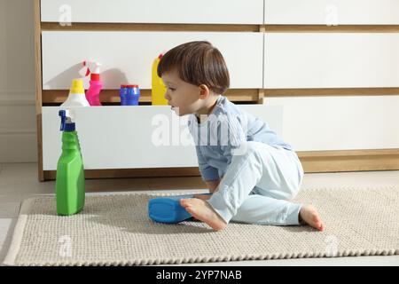 Kleiner Junge, der mit Waschmittelflaschen in der Nähe des Schranks zu Hause spielt. Kind in Gefahr Stockfoto