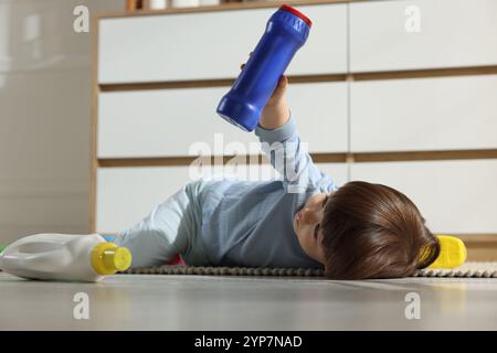 Kleiner Junge, der mit Waschmittelflaschen in der Nähe des Schranks zu Hause spielt. Kind in Gefahr Stockfoto