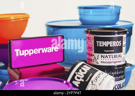 In dieser Fotoabbildung befindet sich ein Stapel verschiedener Kunststoffprodukte neben einem Smartphone mit dem Tupperware-Logo Stockfoto