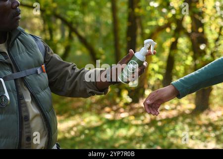 Mittlere Nahaufnahme eines nicht erkennbaren Mannes, der Mückenspray hält und bereit ist, es auf die Kinderhand zu sprühen Stockfoto